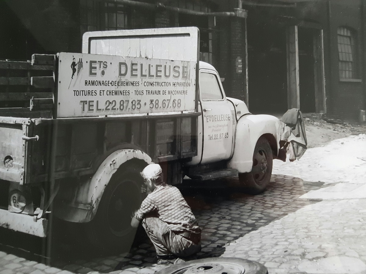 Photo noir et blanc d'un couvreur agenouillé à côté d'un camion Ets Delleuse